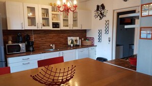 A modern kitchen with white cabinets, a wooden countertop, a red chandelier, and a dining table with a wire rack. - Charming cottage "La Casa Céline", near the sea (Surtainville)