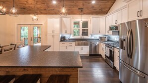 Uma cozinha moderna com armários brancos, uma ilha grande com banquetas, eletrodomésticos de aço inoxidável e iluminação pendente.