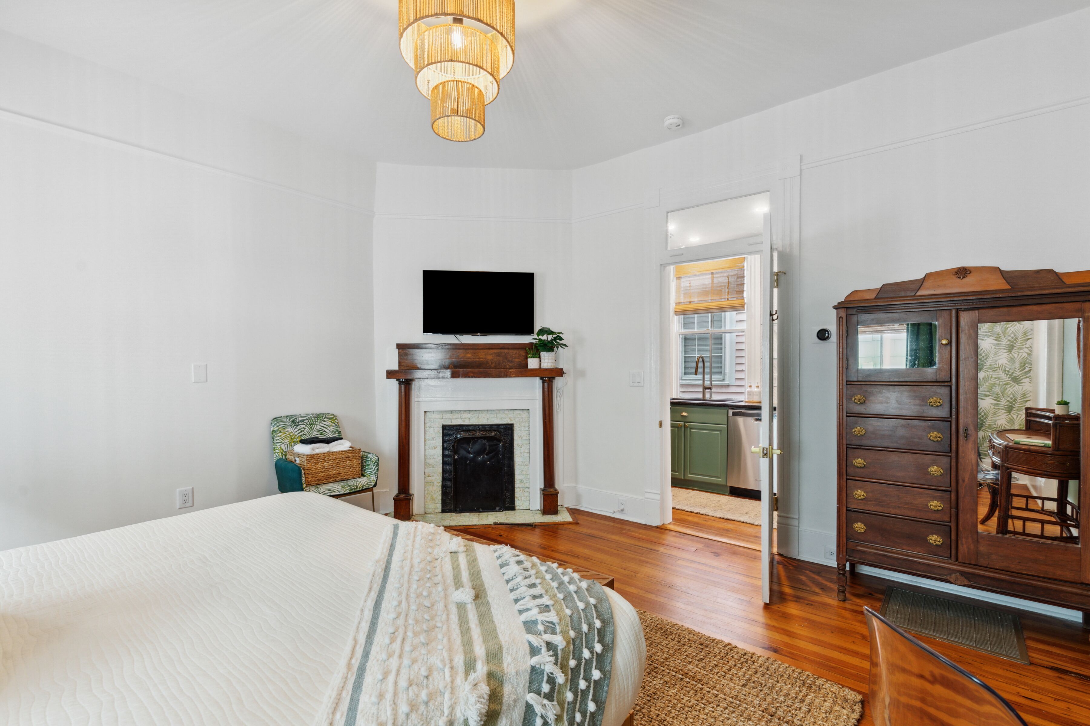 A bedroom with a bed, a television mounted above a fireplace, a wooden dresser, and a door leading to a balcony.