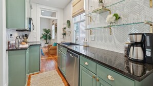 A kitchen with green cabinets, a black countertop, and a herringbone-patterned backsplash. - The Isla Suite: A Dream Getaway for Friends (Charleston)