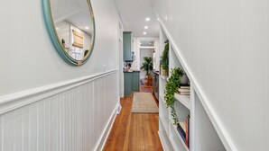 A hallway with white walls, a wooden floor, a mirror, and a staircase leading to a kitchen area. - The Isla Suite: A Dream Getaway for Friends (Charleston)