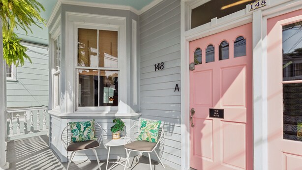 A porch with two chairs, a small table, and a pink door with the number 148A. - The Isla Suite: A Dream Getaway for Friends (Charleston)