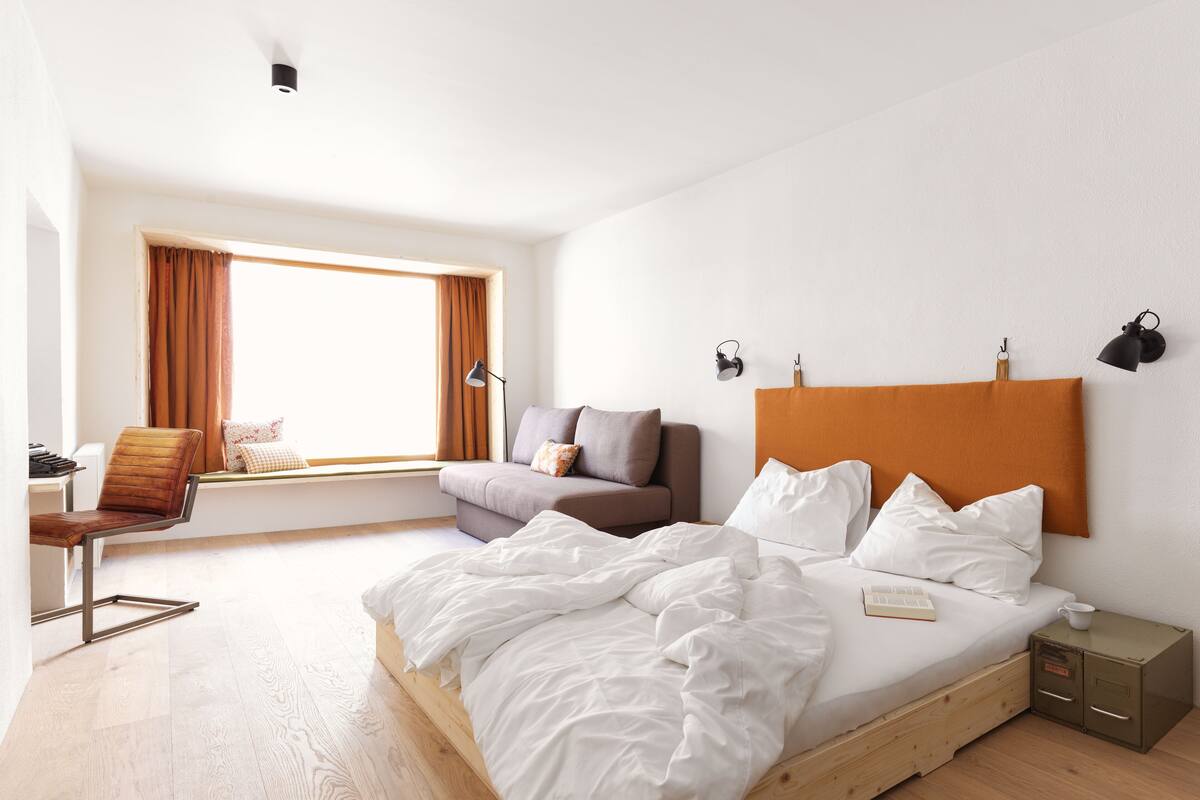 A bedroom with a bed, a sofa, a chair, a desk, and a window with curtains.