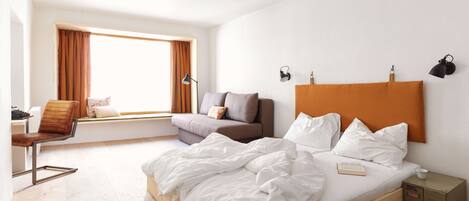 A bedroom with a bed, a sofa, a chair, a desk, and a window with curtains.