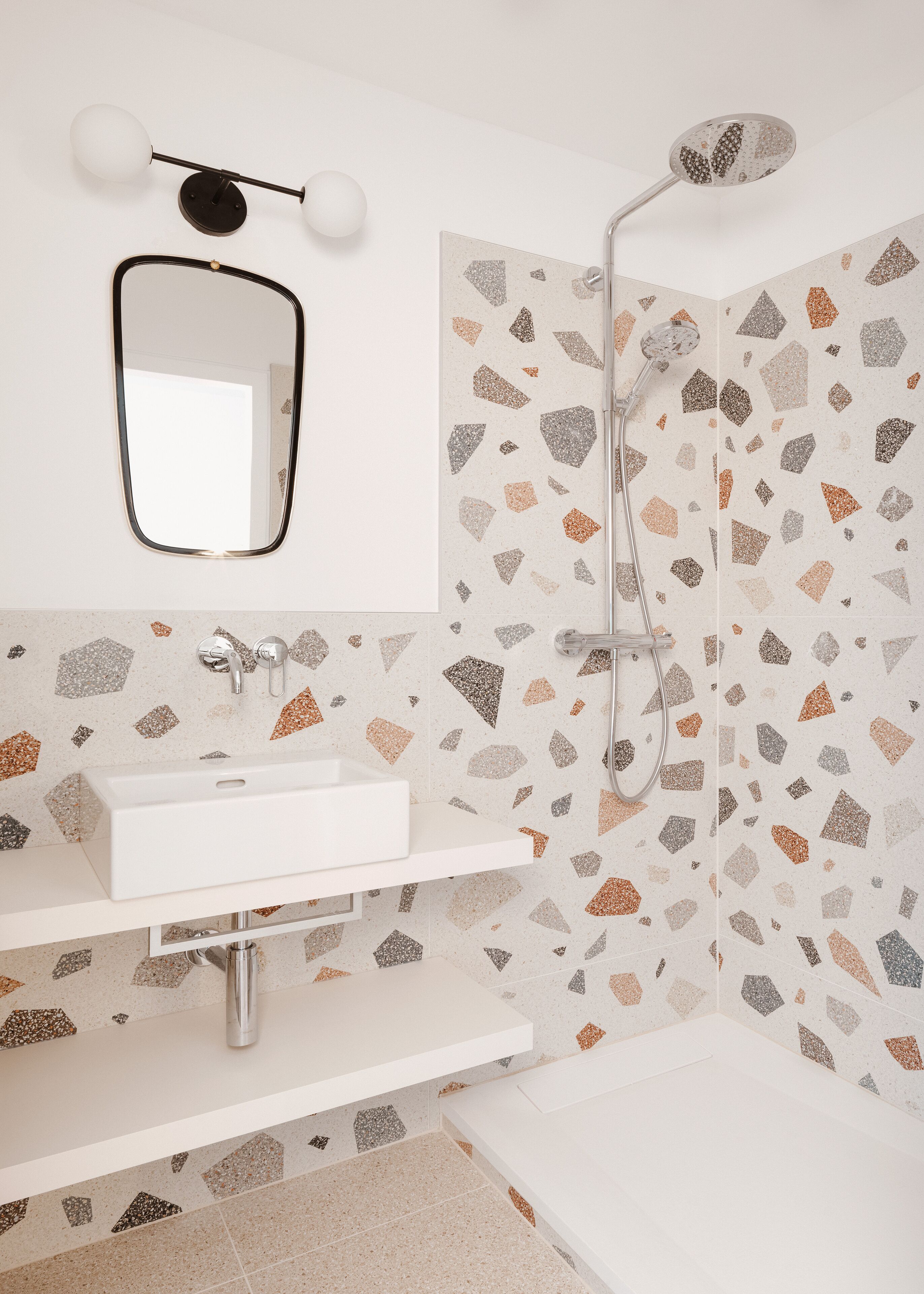 Un baño moderno con un lavamanos blanco, un espejo y una ducha con cabezal de lluvia.