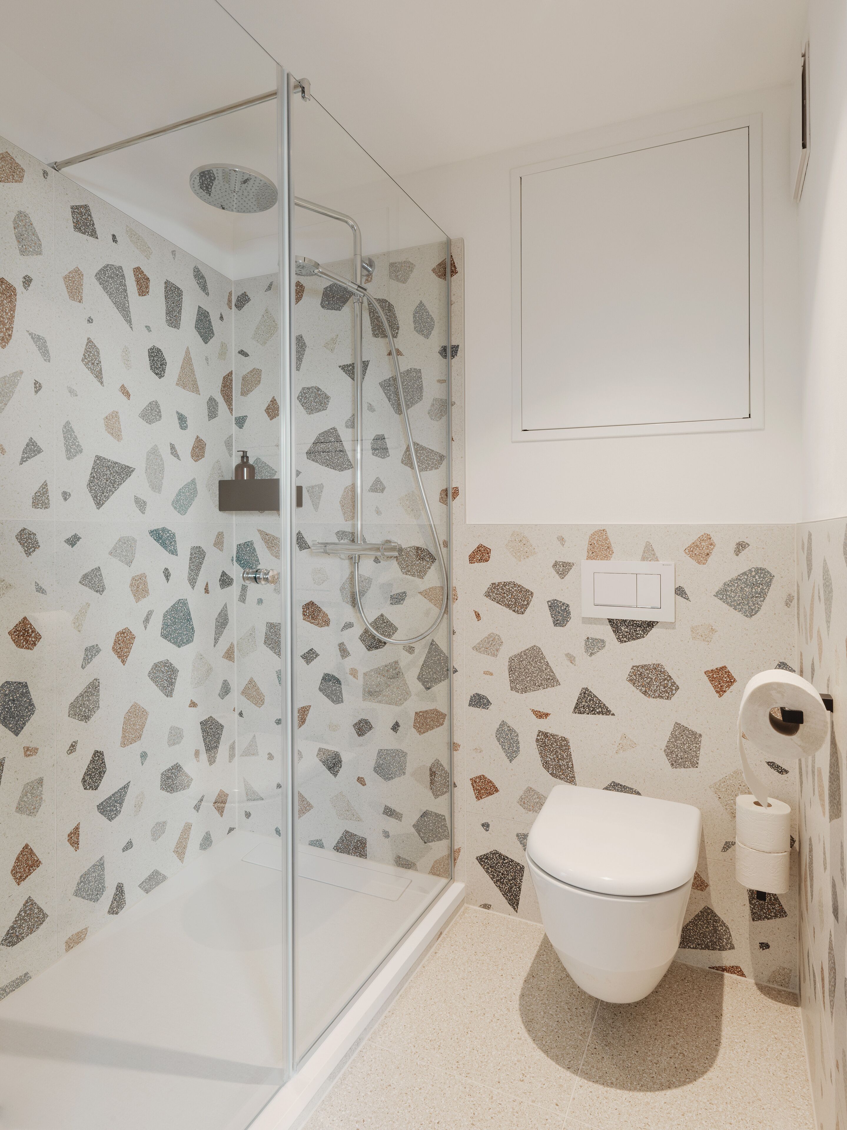Un baño con ducha de vidrio, inodoro y dispensador de papel higiénico en la pared.