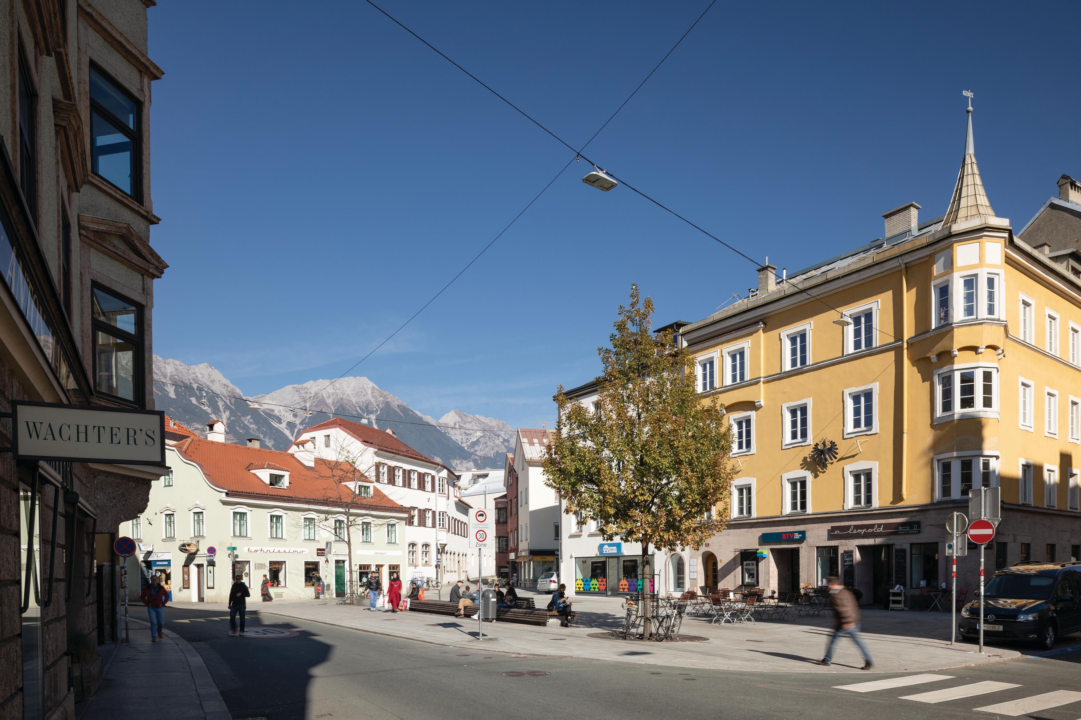 Vista de una calle con edificios, un árbol y un paso de peatones.