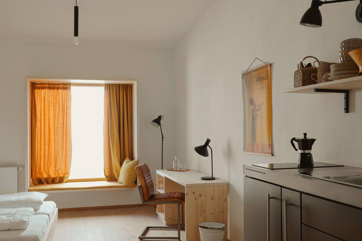 A modern kitchen with wooden cabinets, a built-in bench, and a window with curtains.
