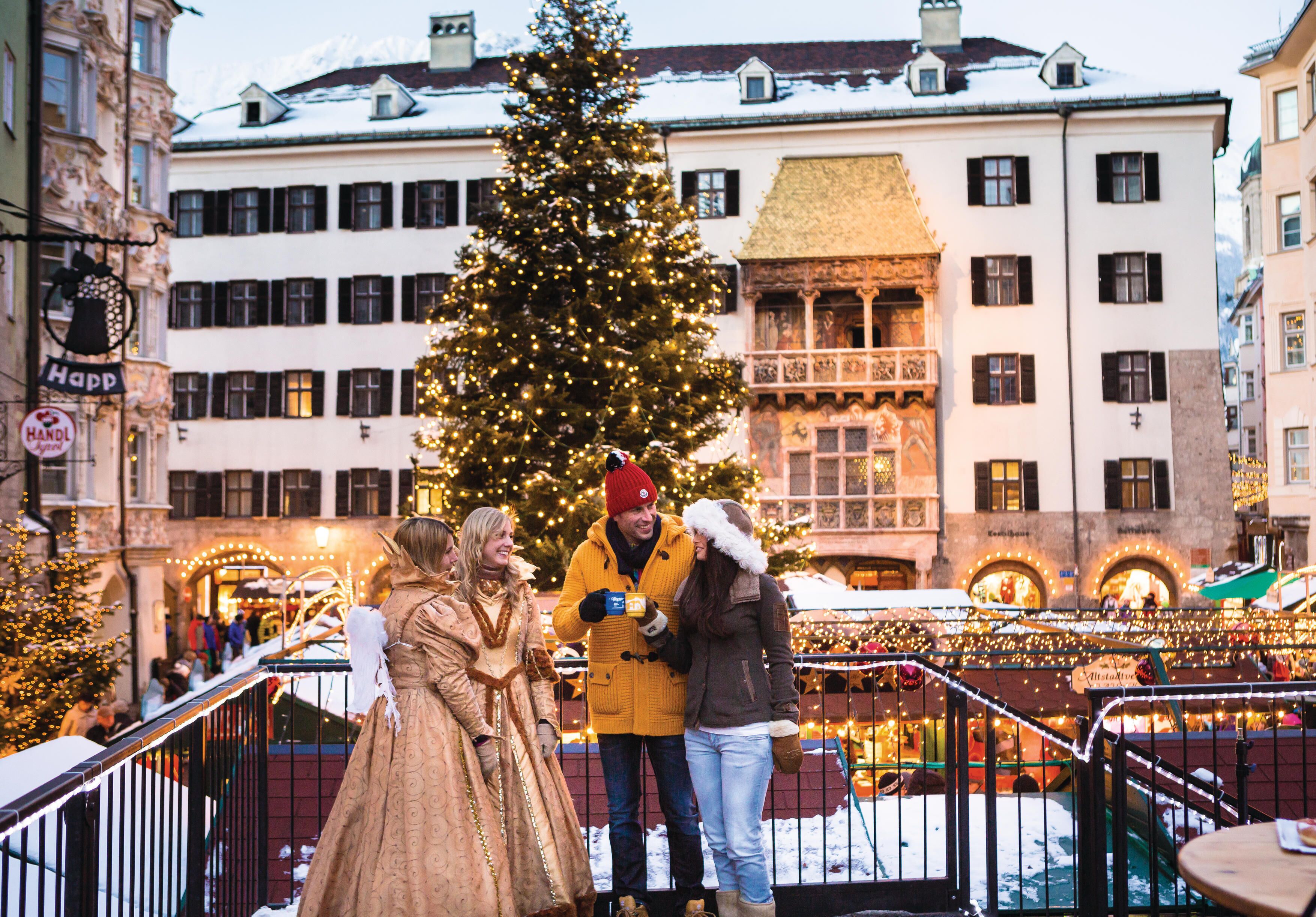A festive market scene with a large Christmas tree and people in winter clothing.