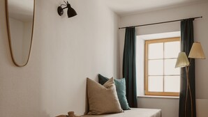 A minimalist bedroom with a single bed, a small stool, a floor lamp, and a large window with curtains. - Urban Inn (Innsbruck)