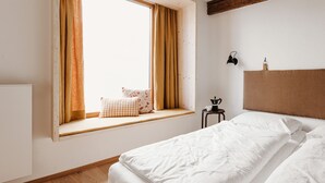 A bedroom with a large window, a bed with white linens, a small bedside table with a coffee pot, and a headboard. - Urban Inn (Innsbruck)