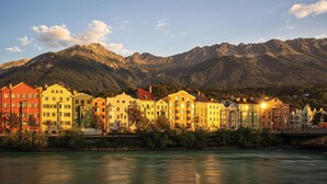 A row of colorful buildings along a river with mountains in the background. - Urban Inn (Innsbruck)
