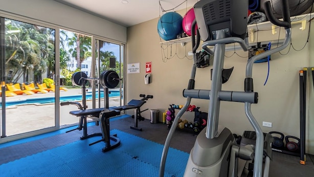 A gym with exercise equipment, a bench, and a view of a swimming pool. - Villa-style 2BR Condo w Pool, GYM Pass near Beach (Noord)