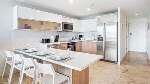 A modern kitchen with white cabinetry, a central island with seating, and stainless steel appliances. - Villa-style 2BR Condo w Pool, GYM Pass near Beach (Noord)
