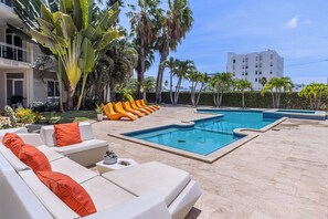 Zona de piscina con sillones de descanso y un edificio blanco al fondo.