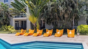 A swimming pool with a tiled edge, surrounded by a row of orange lounge chairs. - Villa-style 2BR Condo w Pool, GYM Pass near Beach (Noord)