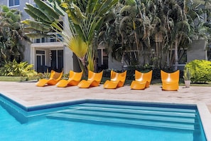 En swimmingpool med en kant av kakel, omgiven av en rad orange solstolar.