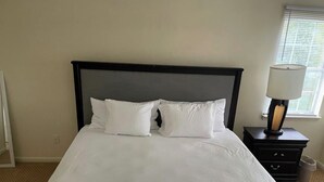 A neatly made bed with white linens and a dark headboard in a room with beige walls. - Cozy home minutes from PNC and Nascar Speedway (Charlotte)