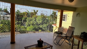 A covered balcony with a glass-top table, wicker chairs, and a potted plant. - Holiday House Second floor Ste (Montego Bay)