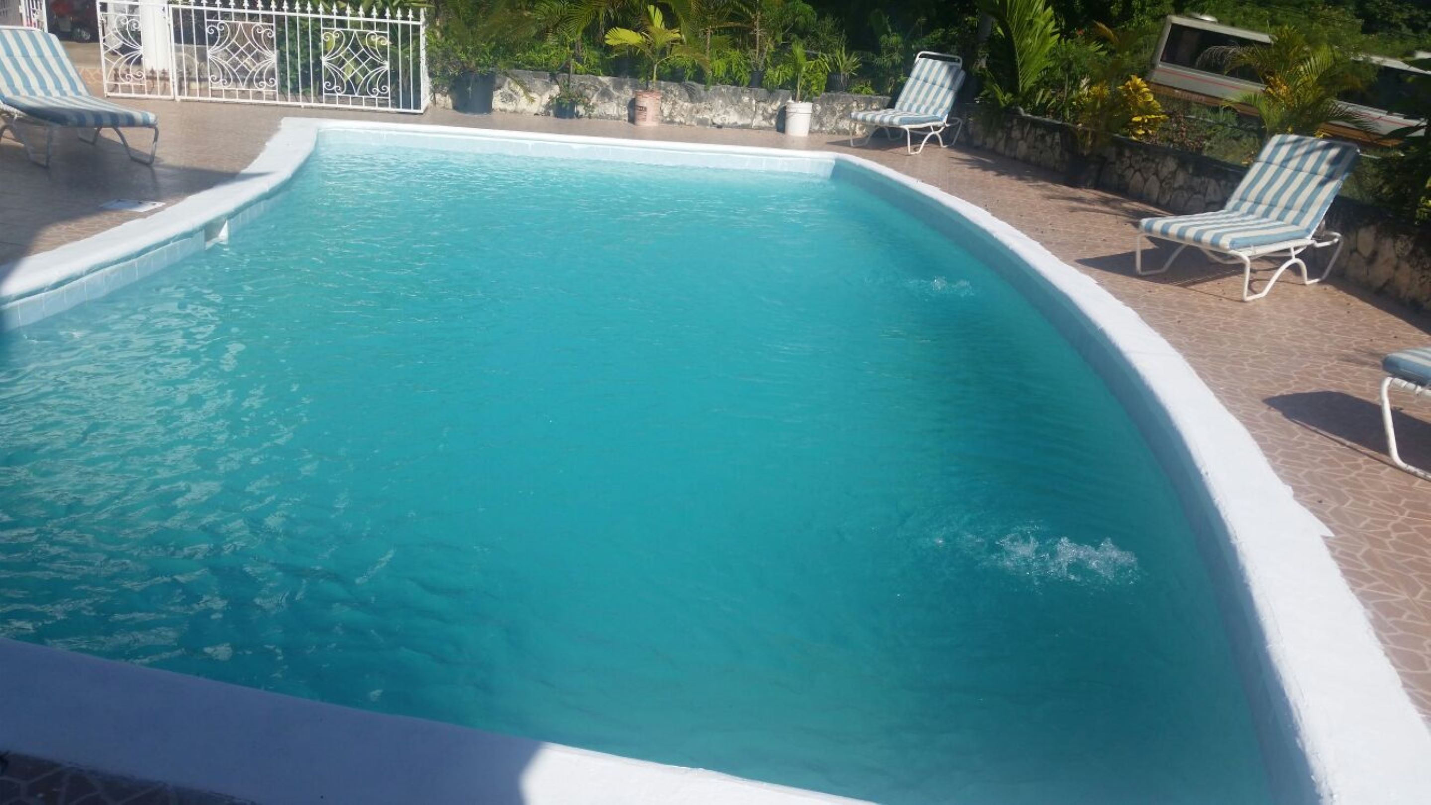 Piscina rectangular con borde blanco, rodeada por un patio de piedra y varias sillas de descanso.