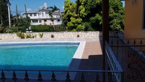 A swimming pool with a stone border, a stone wall, and a large house in the background. - Holiday House Second floor Ste (Montego Bay)
