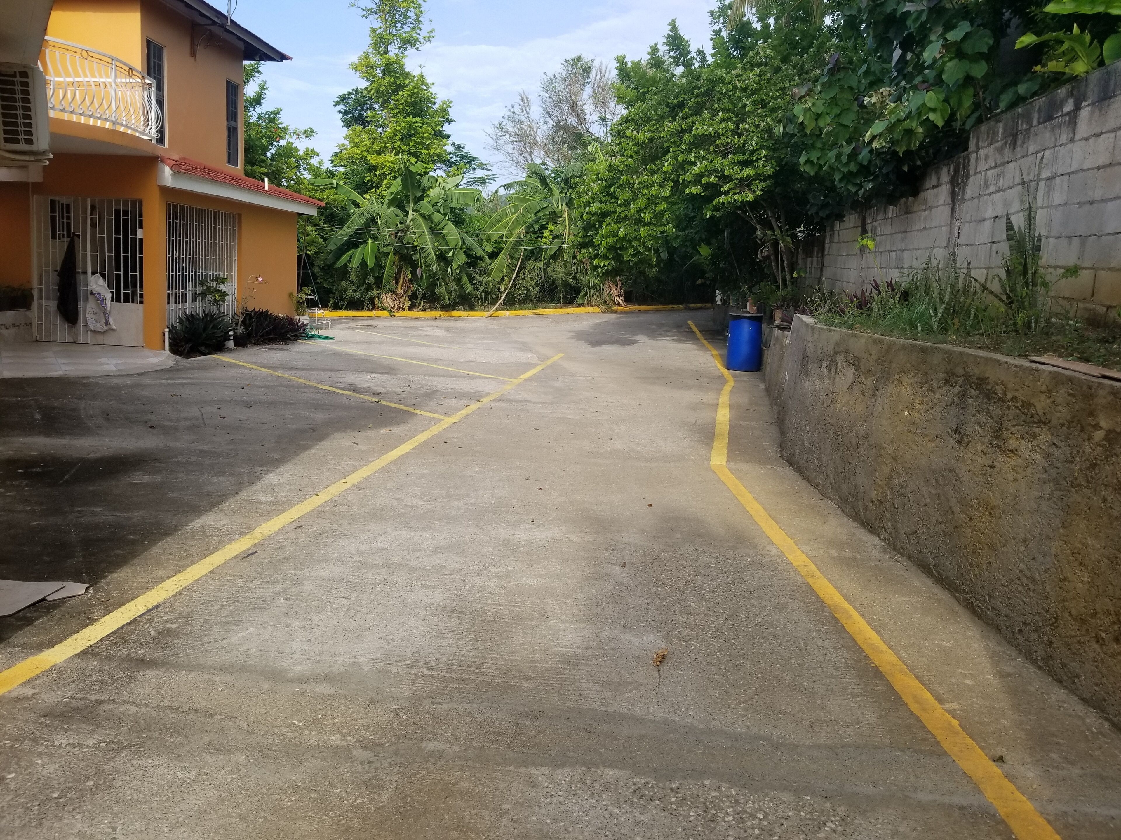 A parking area with yellow lines, a concrete wall, and a building with barred windows.