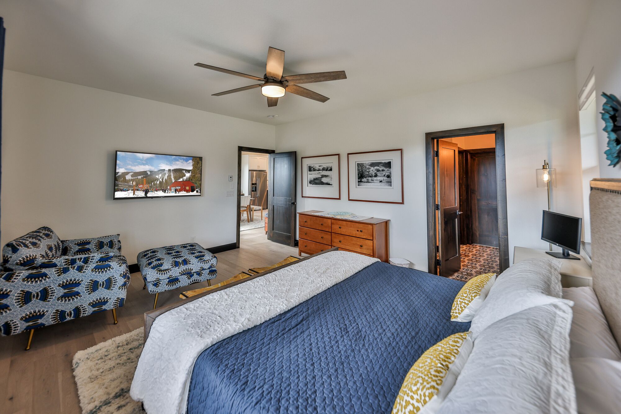 A bedroom with a bed, two chairs, a dresser, and a ceiling fan.