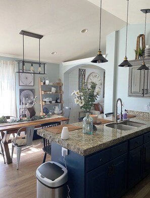 A modern kitchen with a large island, pendant lighting, and a built-in sink. - Cozy Cottage Style Home In The Perfect Location (Idaho Falls)