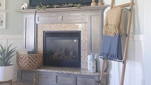 A living room with a fireplace, a mounted television, and a ladder leaning against the wall. - Cozy Cottage Style Home In The Perfect Location (Idaho Falls)