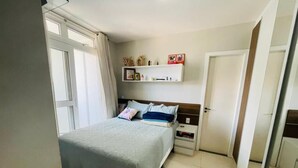 A bedroom with a bed, a nightstand, a shelf with personal items, and a door.