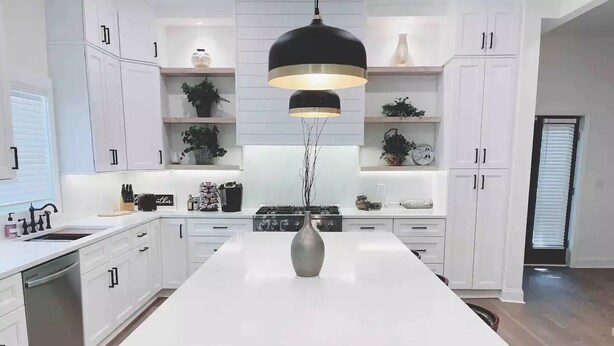 Uma cozinha moderna com armários brancos, uma ilha central e uma luminária pendente preta.