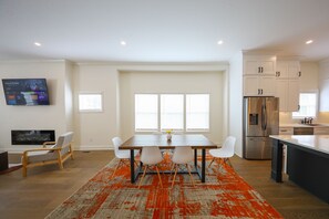 Une cuisine moderne avec des meubles blancs, un réfrigérateur en acier inoxydable et un coin repas comprenant une table en bois et des chaises blanches.