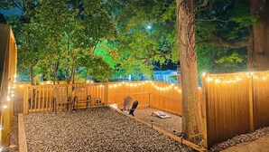 Um deck de madeira com luzes de cordão, uma árvore e um espaço de estar com cadeiras e uma mesa.
