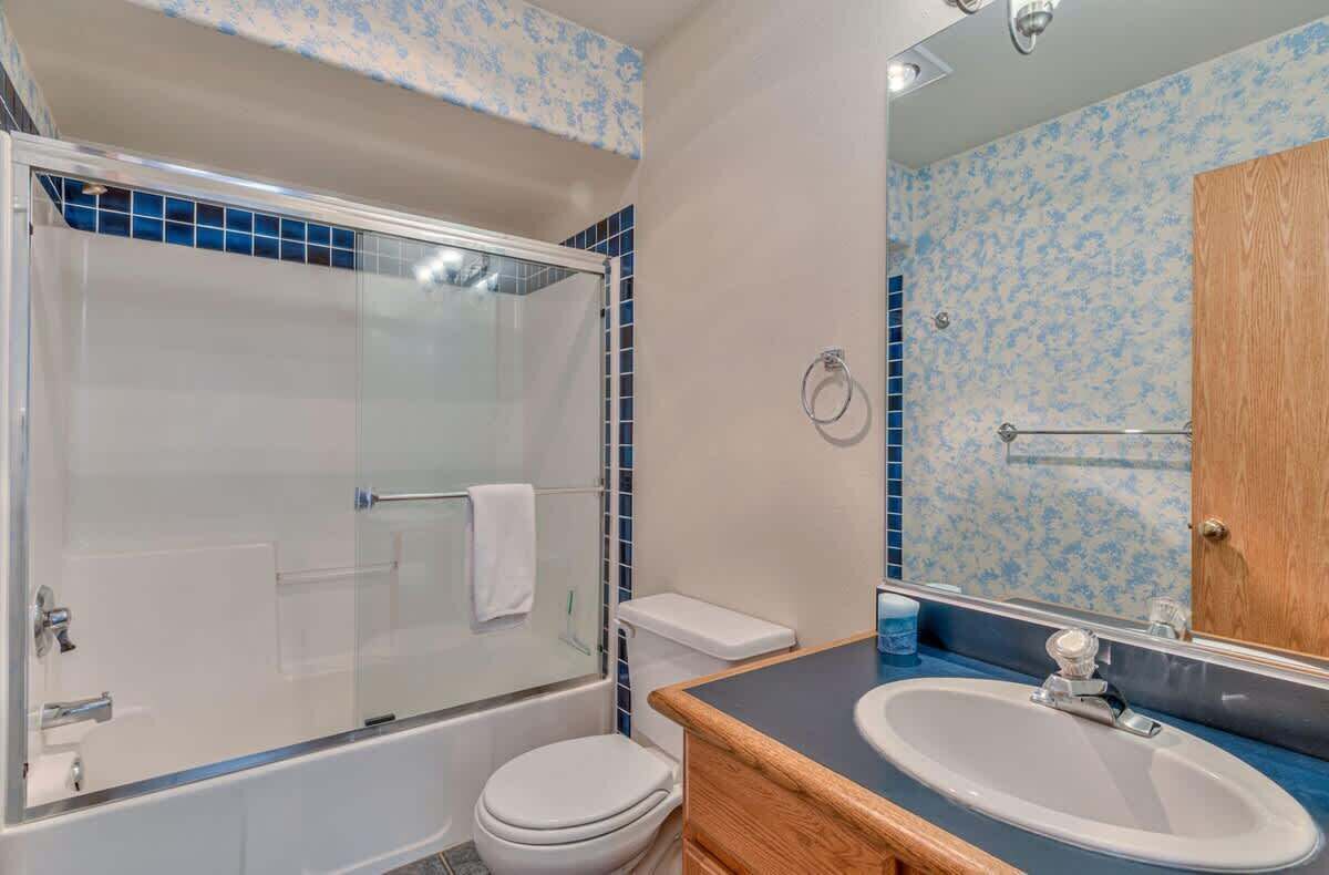 A bathroom with a glass-enclosed shower, a white toilet, a wooden vanity with a sink, and a mirror.