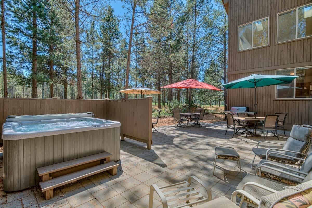 A hot tub, outdoor seating, and a wooden deck with a view of a forest.