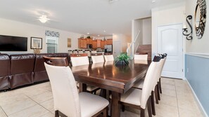 A dining area with a large wooden table, white cushioned chairs, a brown leather couch, and a kitchen in the background. - New Listing! Champions Gate Resort, 10mi to Disney & 21mi to Universal - GRH439019 (Davenport)