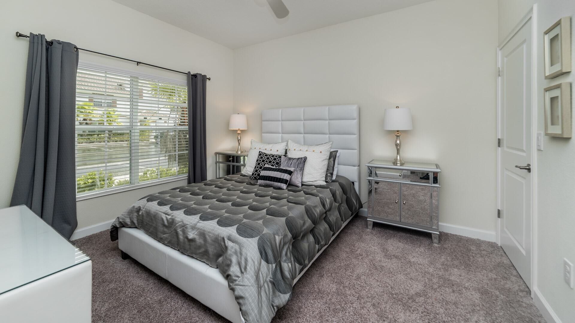 A bedroom with a bed, bedside tables, a nightstand, a window with curtains, and a door.