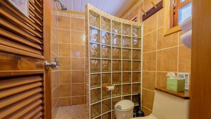 Un baño con cabina de ducha revestida de azulejos, inodoro y tocador de madera con dispensador de toallas.