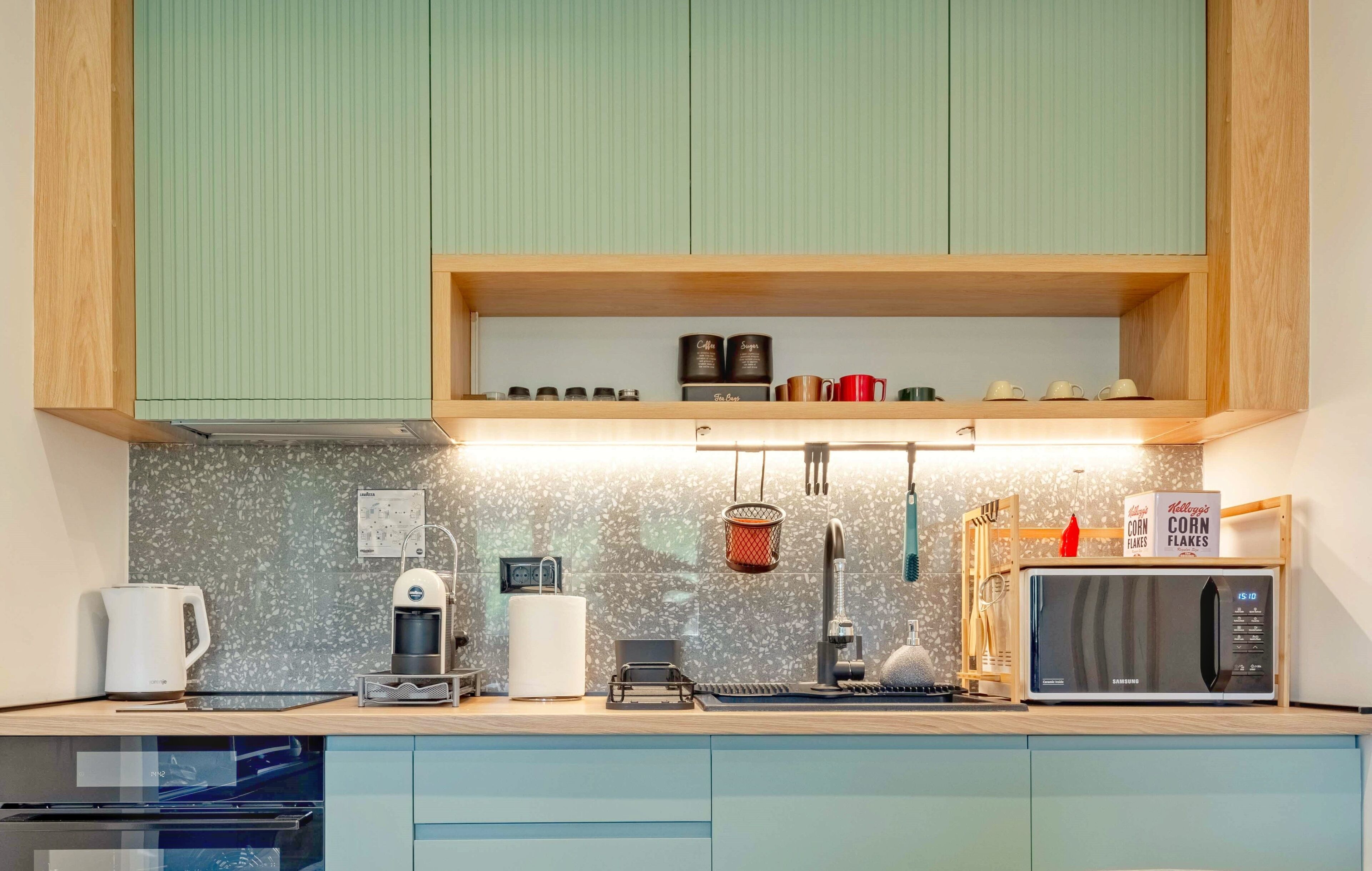 A modern kitchen with a coffee machine, kettle, microwave, and a shelf with various kitchen items.
