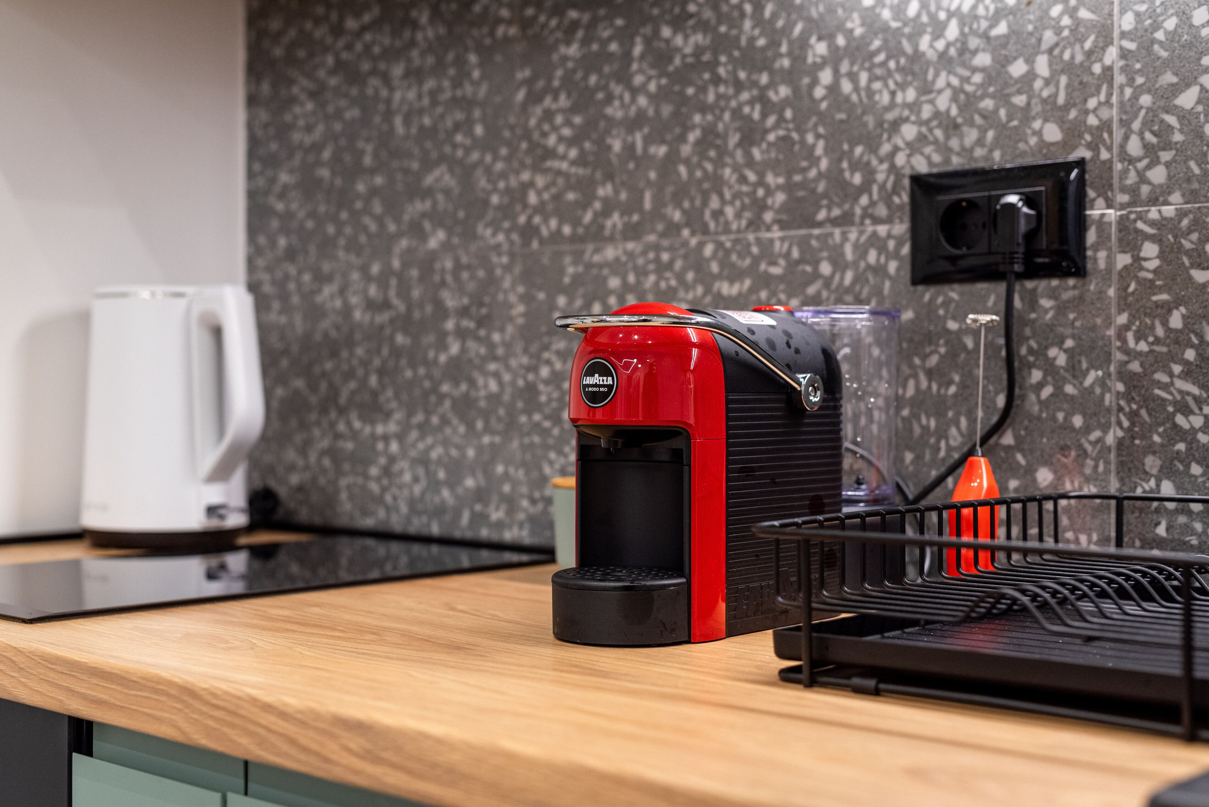 A kitchen with a coffee machine, a kettle, and a power outlet on the wall.