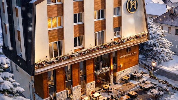 Een modern hotel met een sneeuwbedekte dak, een restaurant op de begane grond, en zicht op een besneeuwd dorpje op de achtergrond.