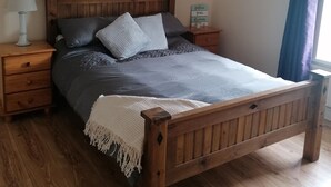 Ein hölzernes Bett mit Kopfteil, ein Nachttisch mit Lampe, eine herzförmige Dekoration und ein Schild mit motivierenden Worten.