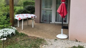 Un'area esterna riparata con un tavolo e un ombrello rosso, una porta in vetro e un vialetto sterrato.