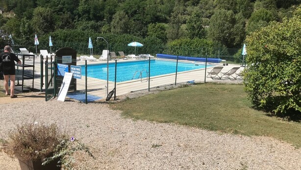 Piscina con area recintata, sedie a sdraio e una persona in piedi vicino al cancello.