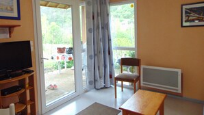 Una stanza con televisione, una sedia, un tavolo e una porta-finestra scorrevole che dà su una zona esterna con una sedia e un tavolo.