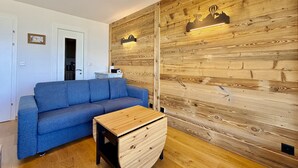 A modern living room with a blue sofa, a wooden coffee table, and a wooden accent wall with a light fixture.