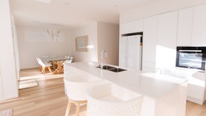 A modern kitchen with white cabinetry, a large island with bar stools, a refrigerator, and a built-in oven.