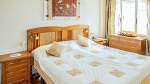 Un dormitorio ordenado con una cama grande, mesitas de noche de madera, un aparador y un cuadro colgado en la pared.
