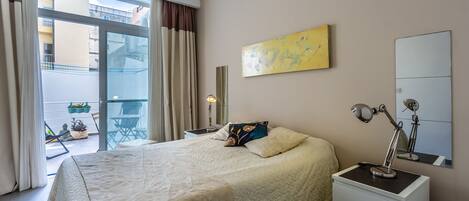 Un dormitorio con una cama grande, una mesita de noche con lámpara, una ventana con cortinas y vistas al balcón exterior.