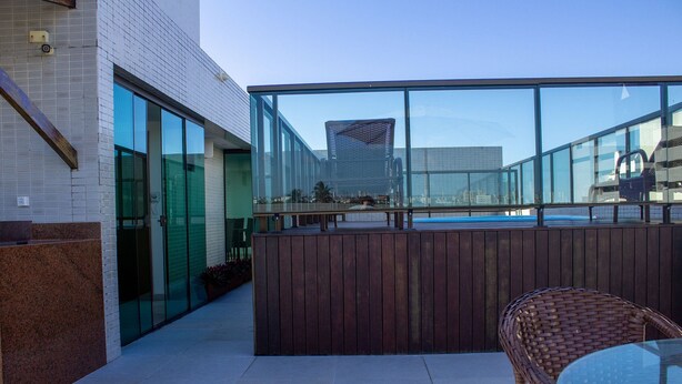 Ein Terrassenbereich im Freien mit Glasgeländer, Korbmöbeln und Blick auf eine Stadtlandschaft.